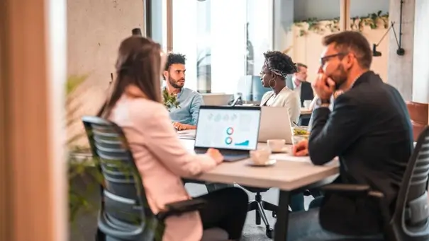 Réunion d’une équipe marketing autour d’une table, un ordinateur portable affichant des graphiques, dans un bureau moderne.